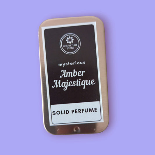 Solid perfume tin labeled 'Mysterious Amber Majestique' on a purple background