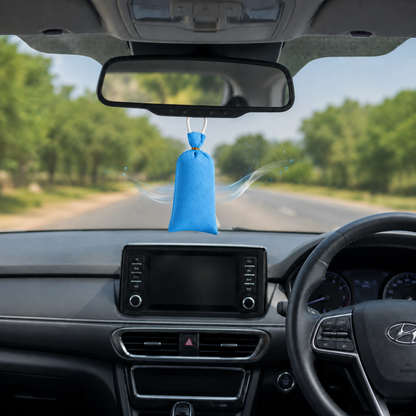 A blue car air freshener bag hanging from the rearview mirror inside a car cabin, with the windshield showing a blurred road and trees outside.